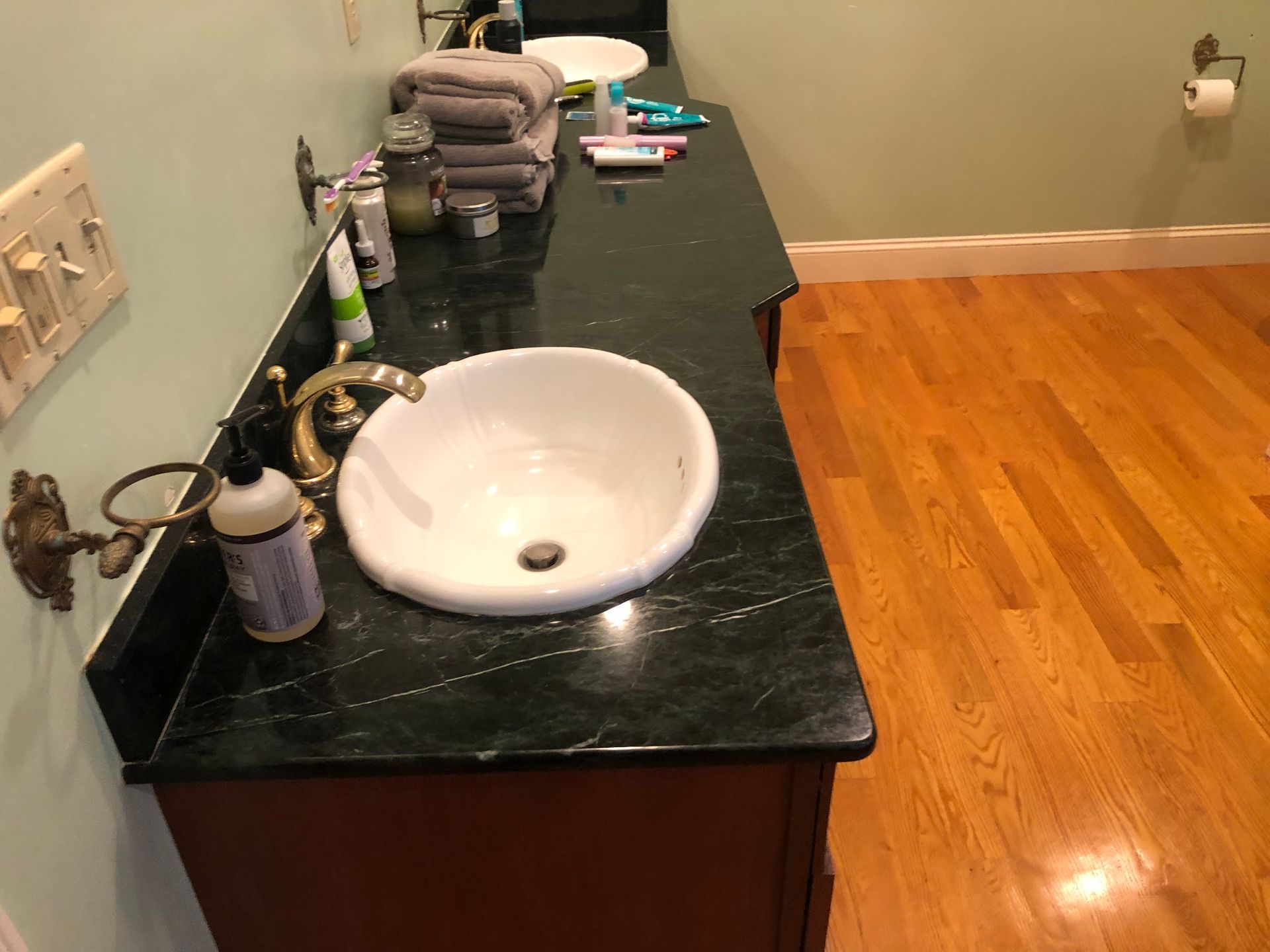 Bathroom vanity with white sink, black countertop, and towels on the counter, next to hardwood floor.