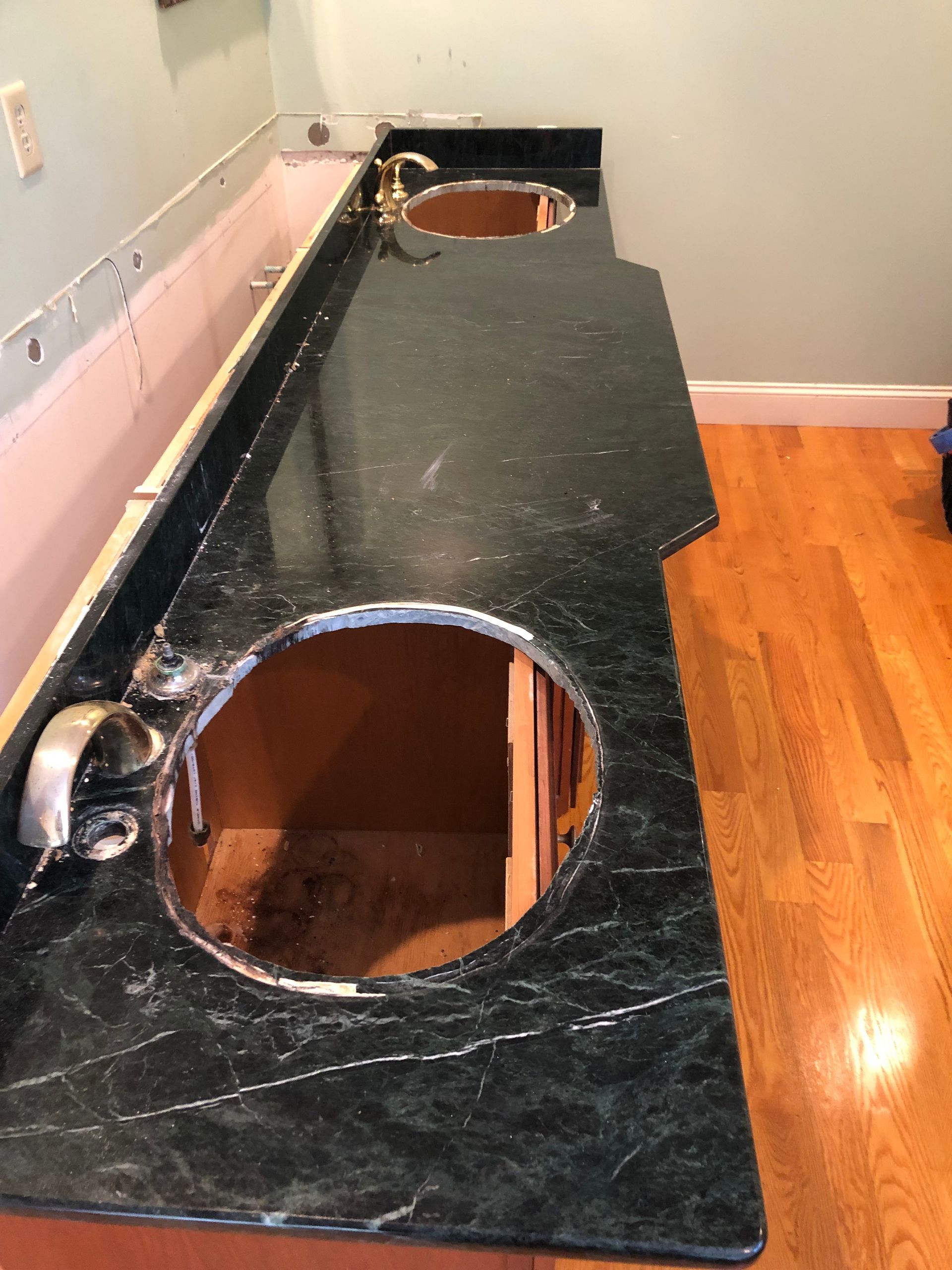 Black bathroom vanity countertop with two circular sink cutouts and an exposed faucet area, under renovation