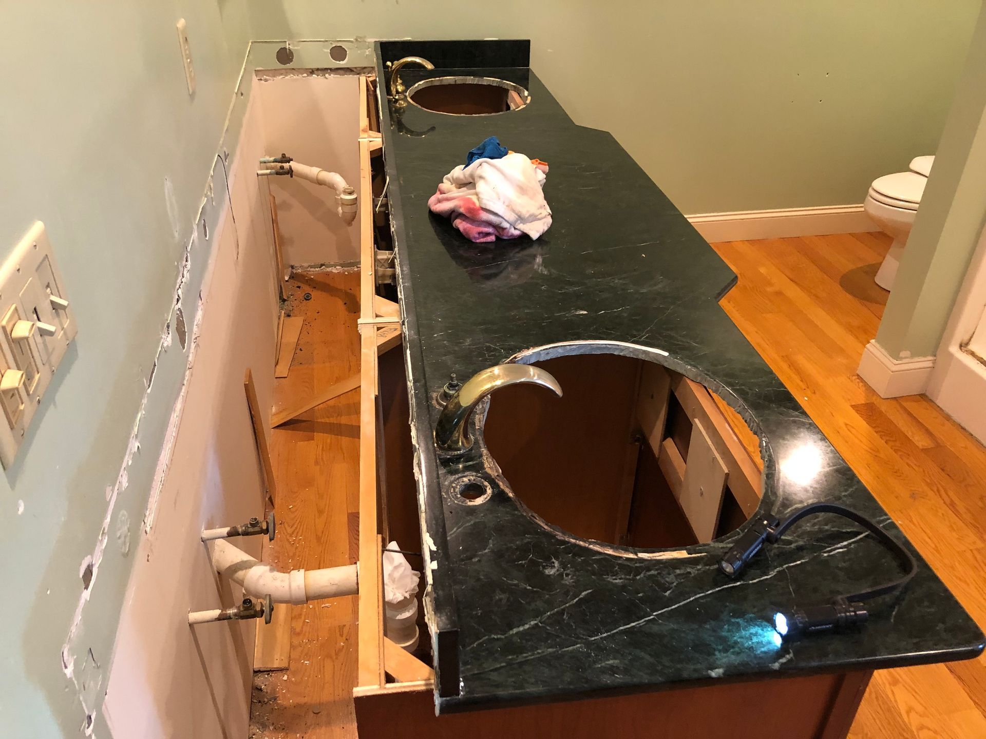 Bathroom vanity countertop with sink cutouts removed, exposing plumbing beneath.