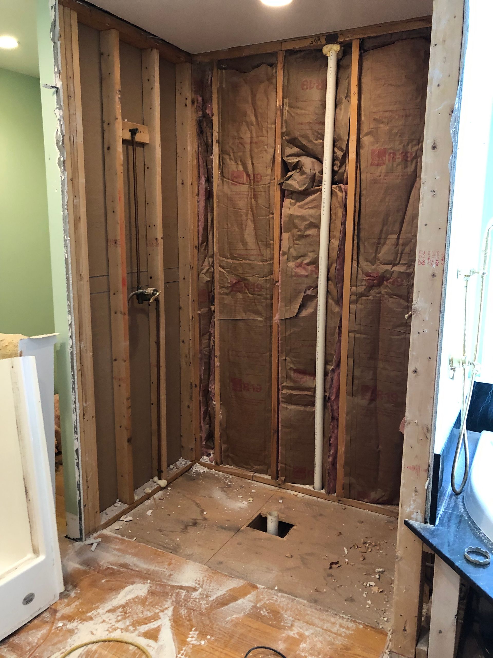 Unfinished bathroom wall with exposed studs, insulation, and subfloor demolition debris.