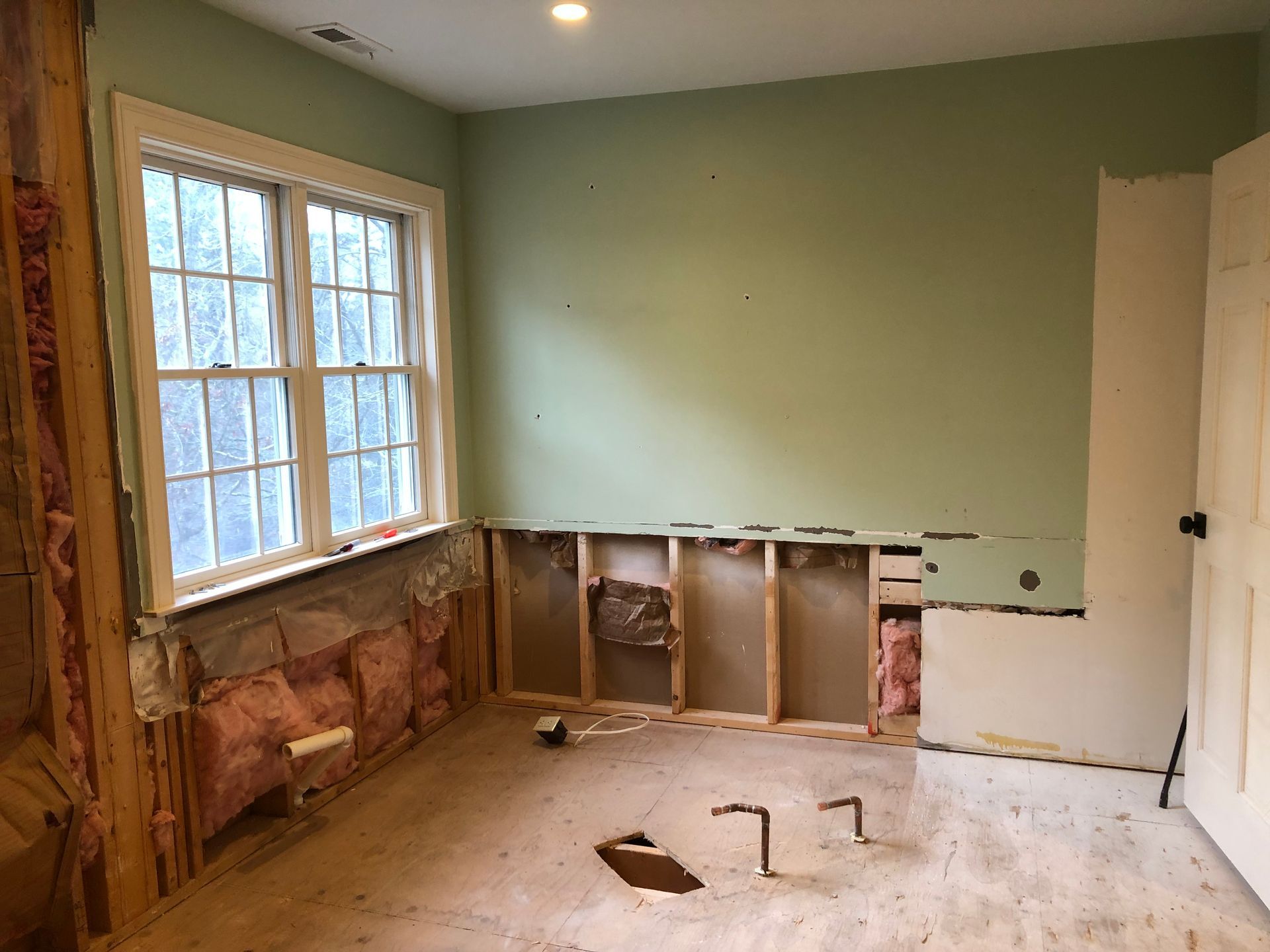 Partially demolished room with exposed wall studs, green walls, and a window on the left.