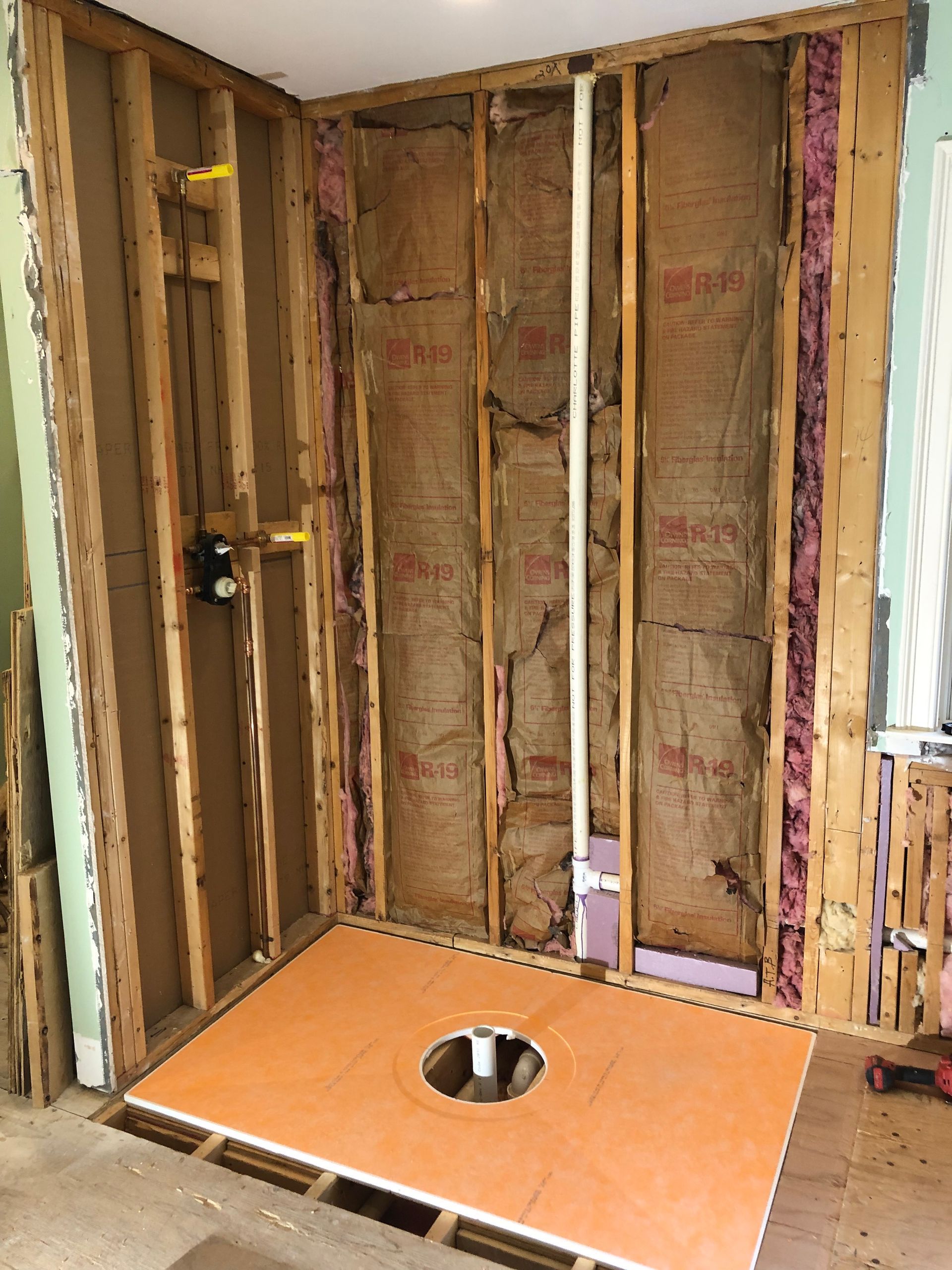 Framed bathroom shower under construction with orange subfloor and plumbing opening.