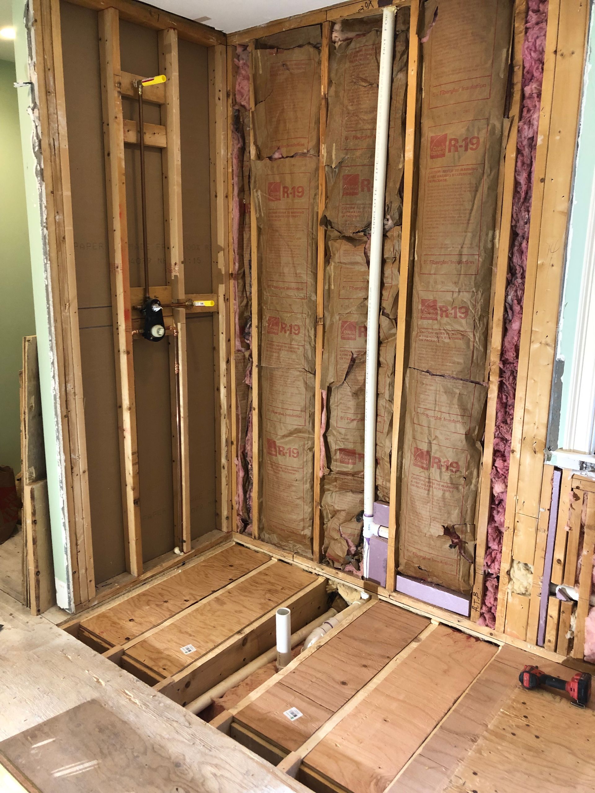 Framed bathroom under renovation with exposed insulation, plumbing, and subflooring