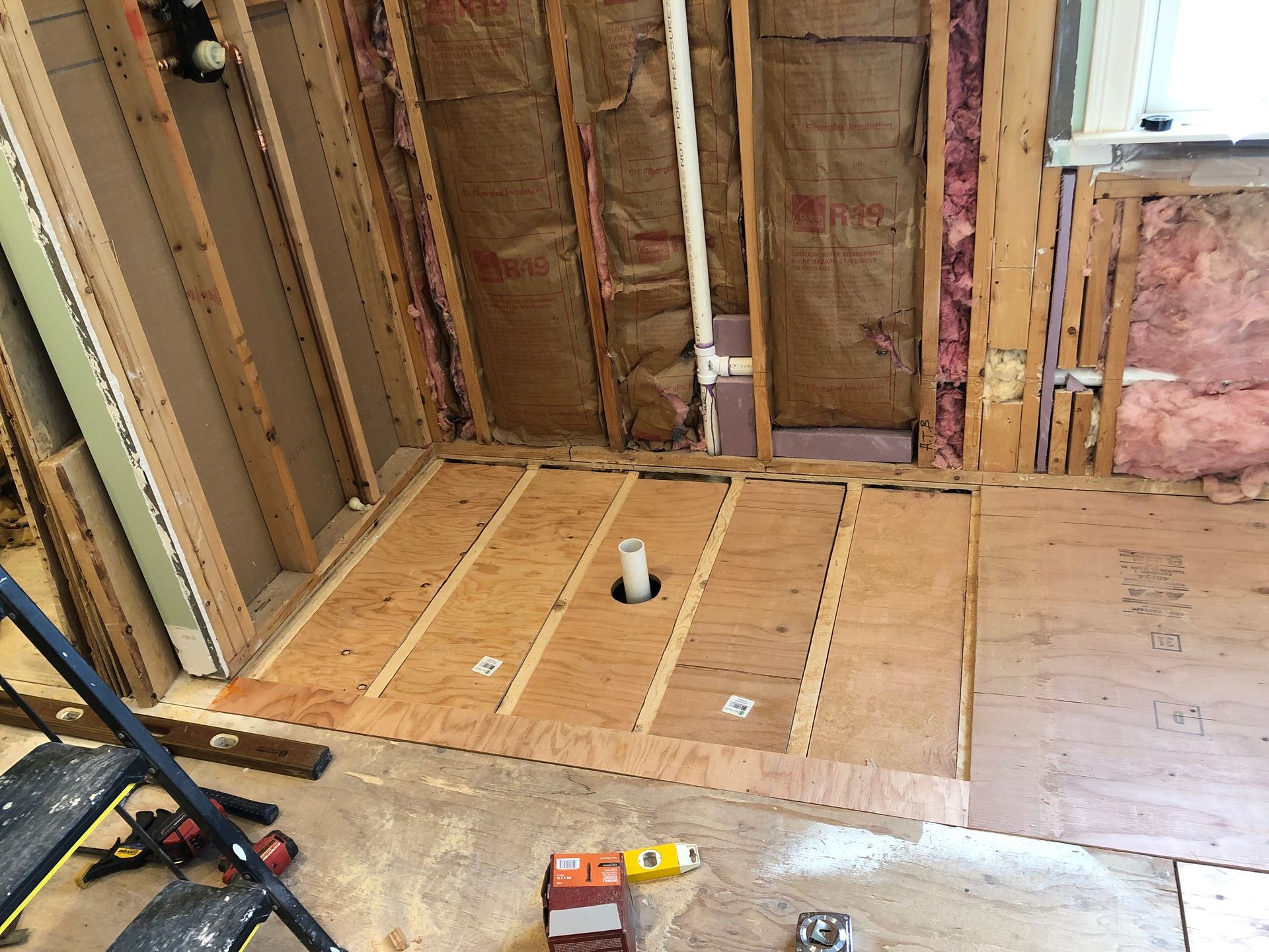 Unfinished room with exposed wall studs, subflooring, and a small work light near a window.