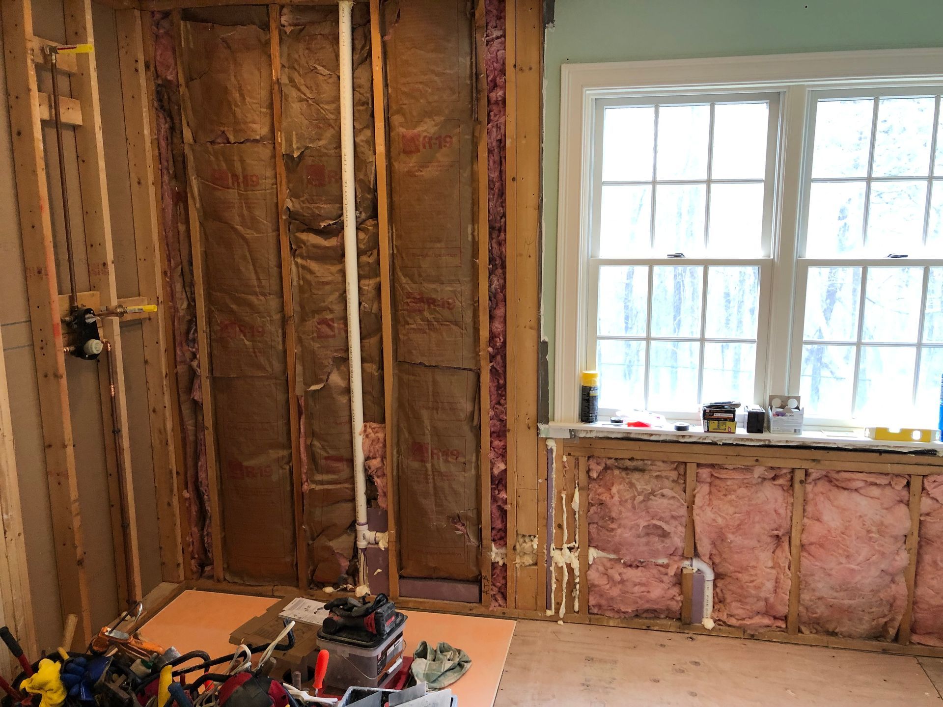 Partially renovated room with exposed insulation, studs, and a bright window above a damaged wall.