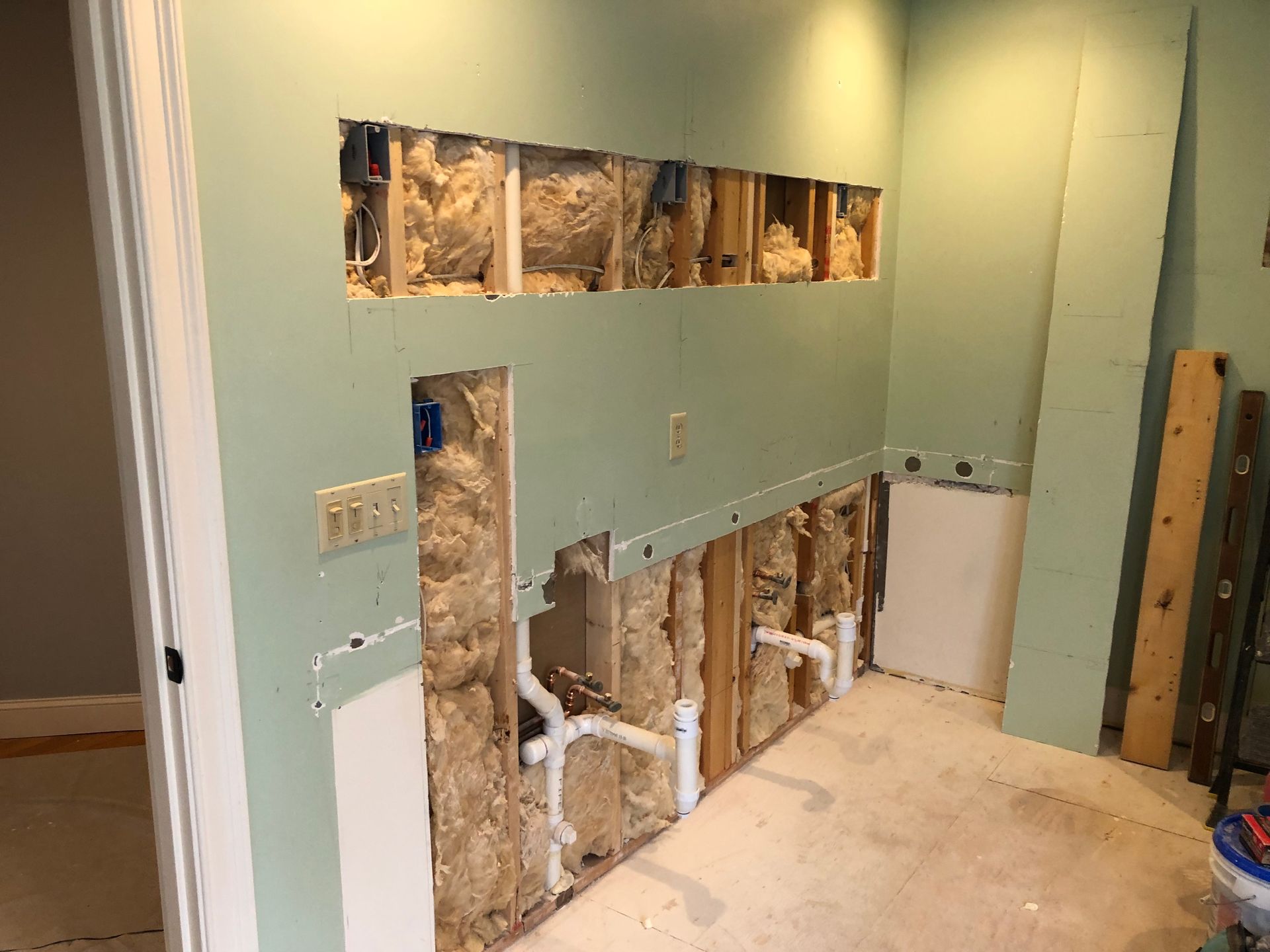 Partially gutted bathroom with exposed studs, pipes, and green walls during renovation