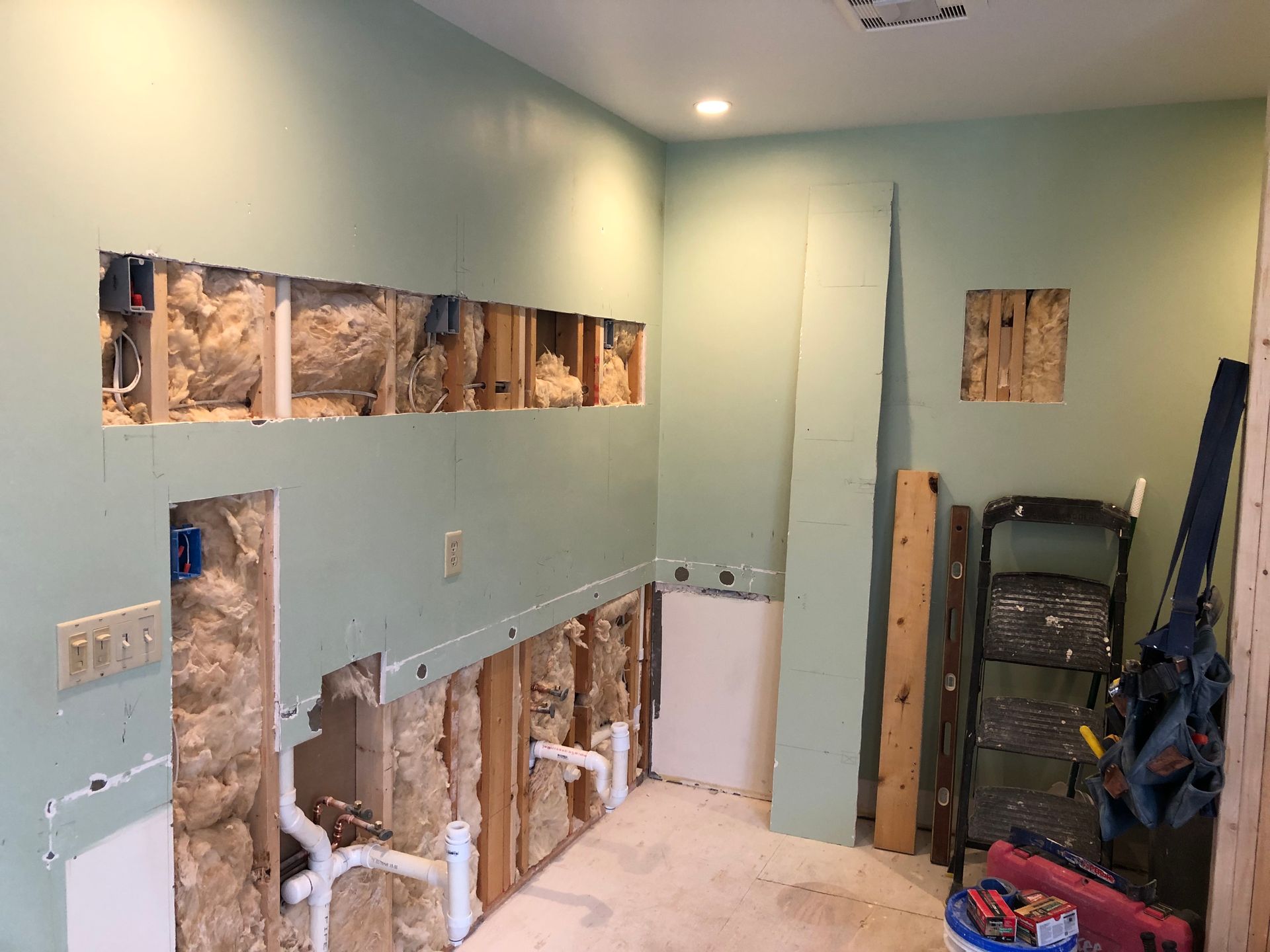 Bathroom under renovation with exposed wall studs, plumbing, and light green painted walls