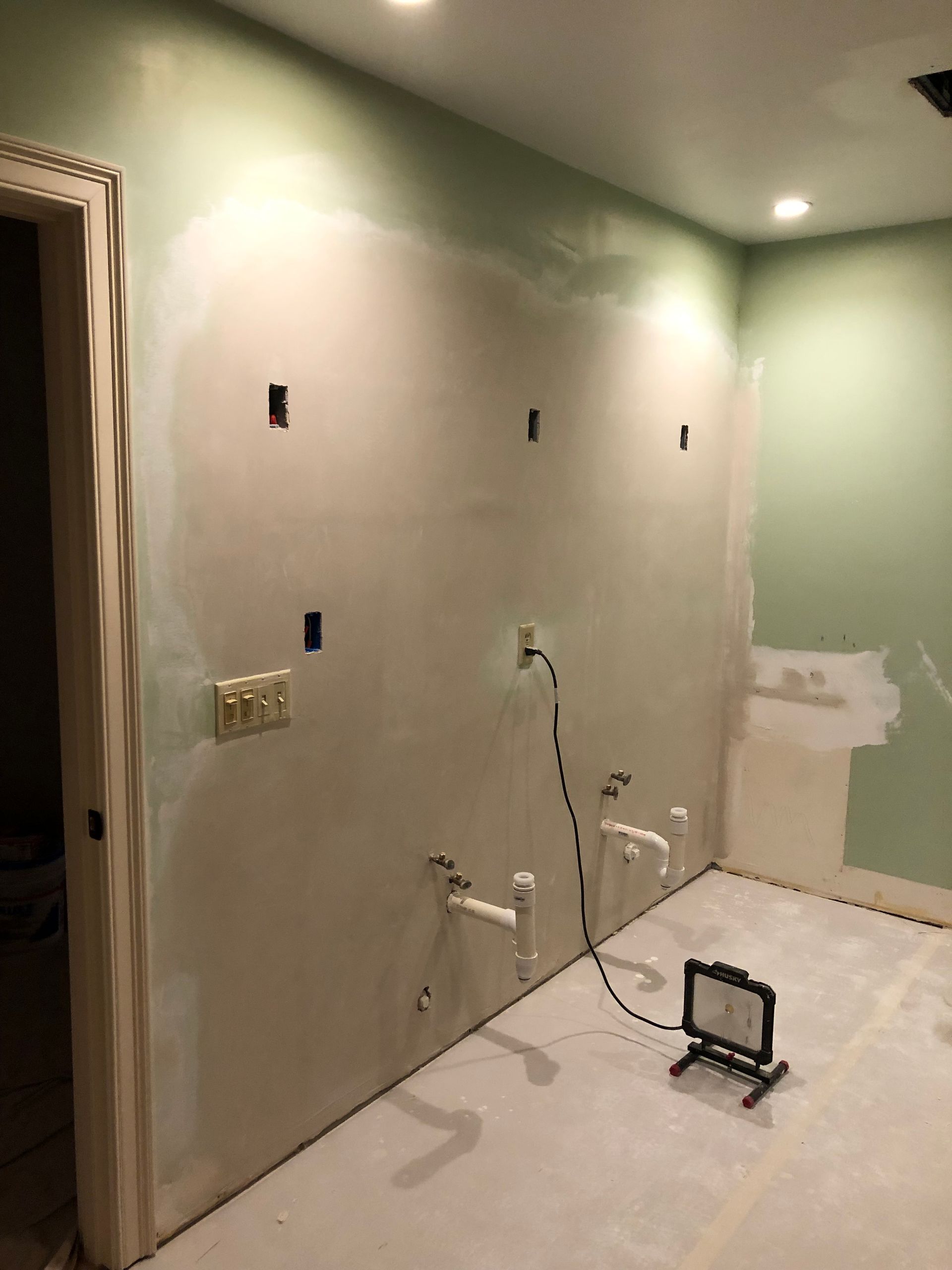 Renovation room with unfinished drywall, wall outlets, and plumbing fixtures beside a covered floor.