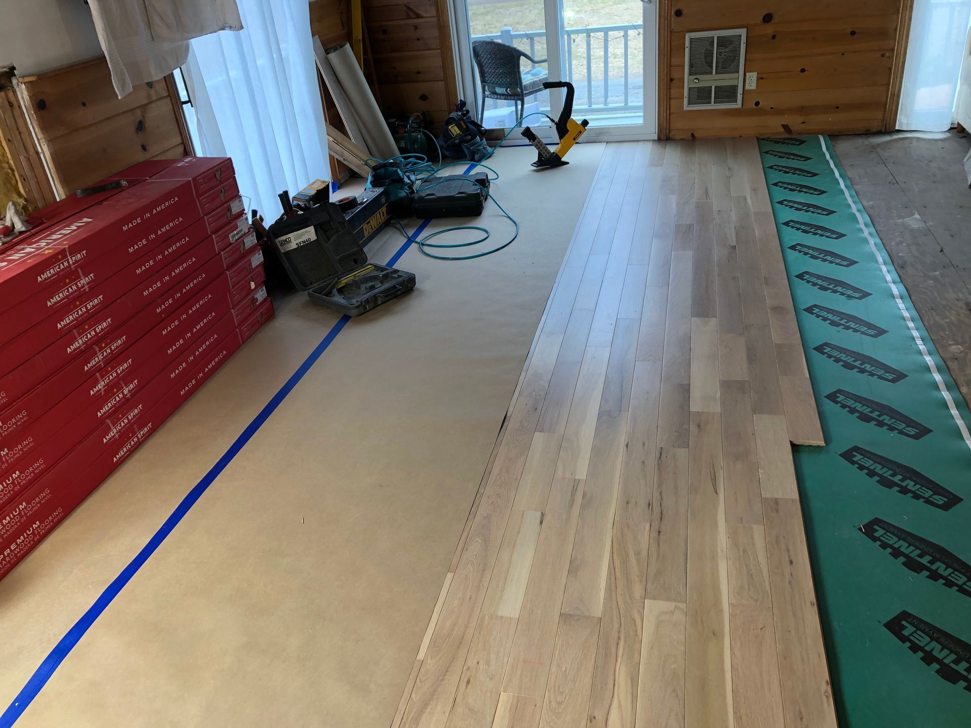 Partially finished wood floor in a cabin interior with tools and a stack of red boxes along the wall
