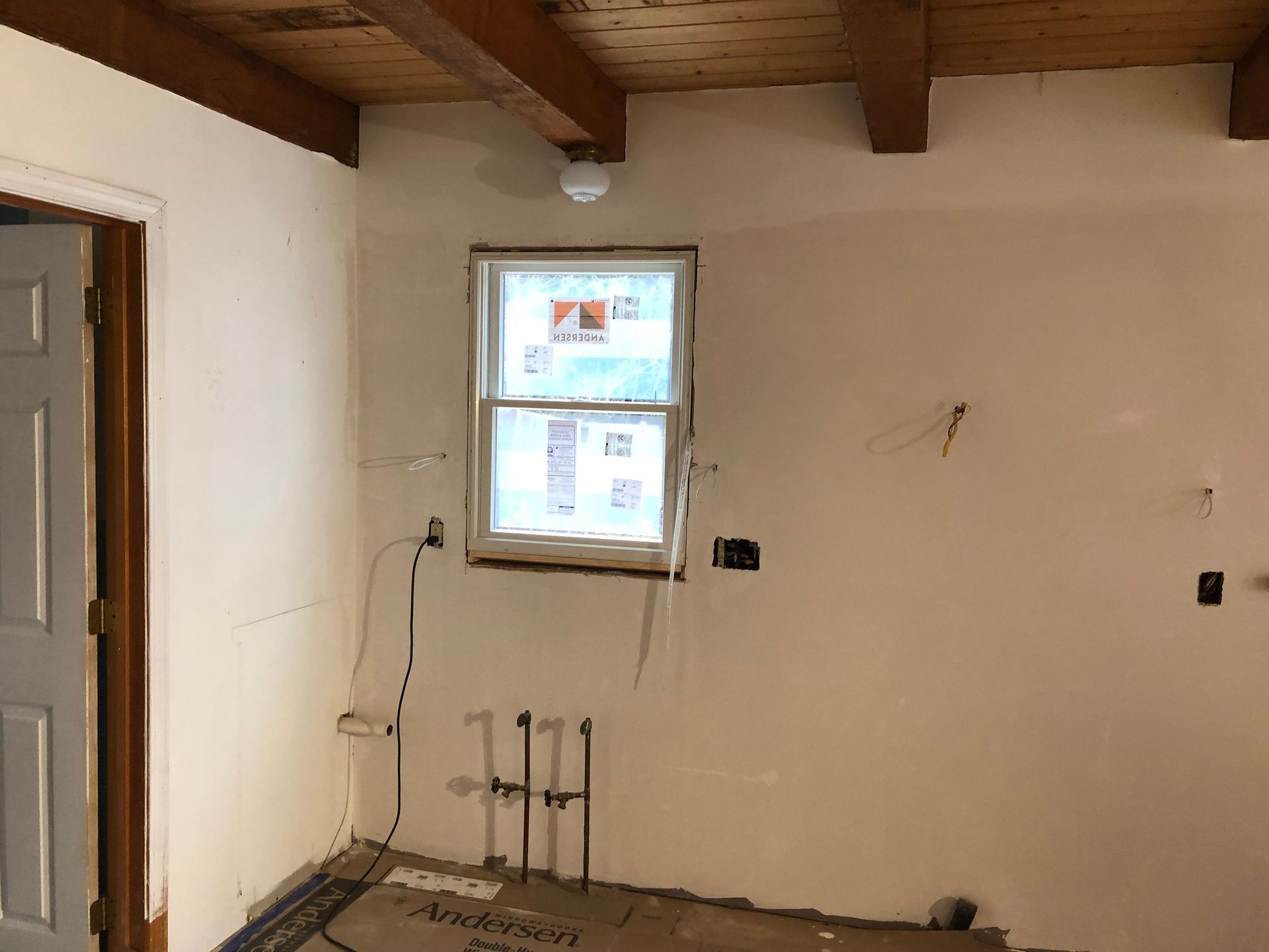 Empty room under renovation with white walls, exposed wood ceiling, and a small window.