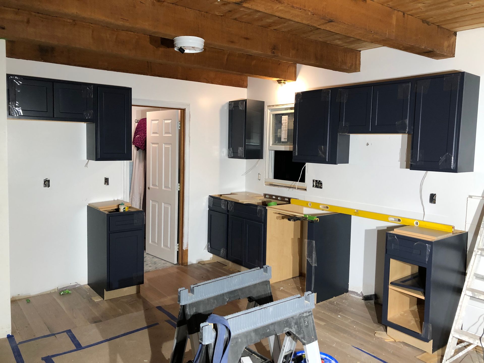 Kitchen under renovation with dark cabinets, exposed beams, and taped-off floor areas