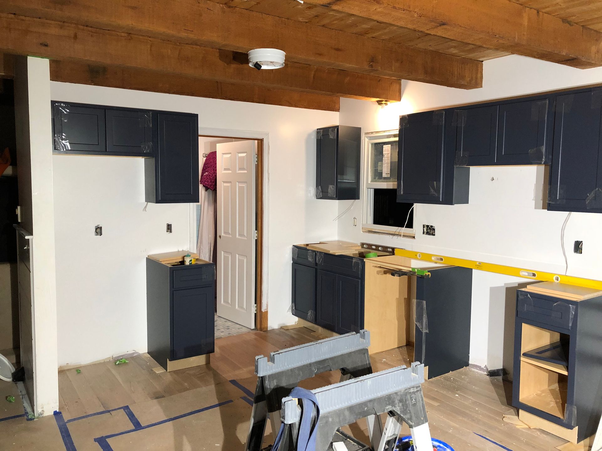 Partially remodeled kitchen with dark cabinets, white walls, exposed beams, and tools on the floor