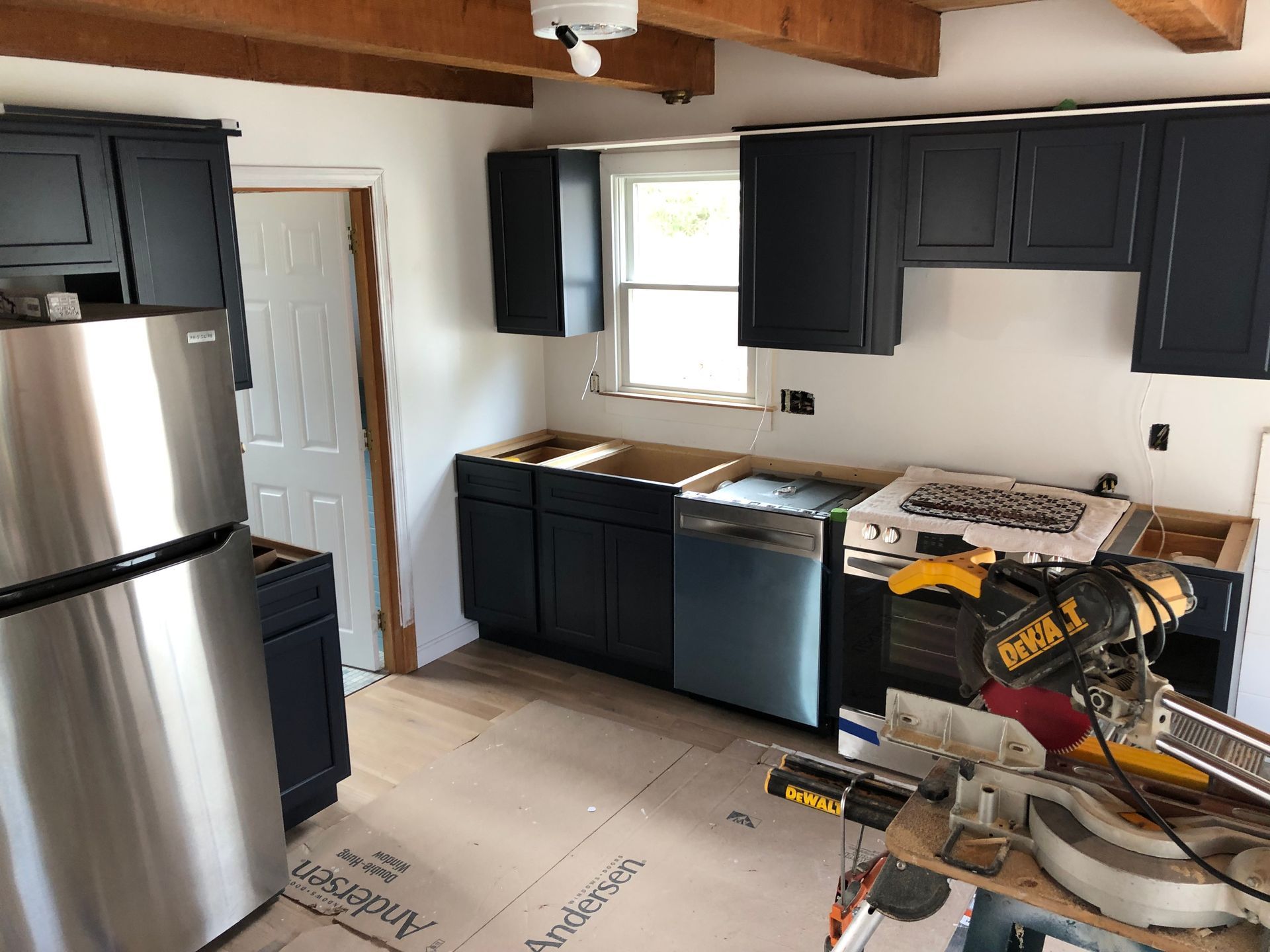 Kitchen under renovation with black cabinets, stainless fridge, and tools on the floor
