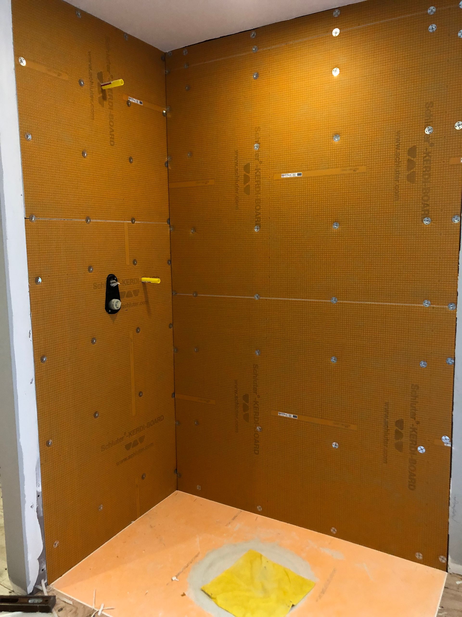 Small unfinished shower stall with orange waterproofed walls and a floor drain.
