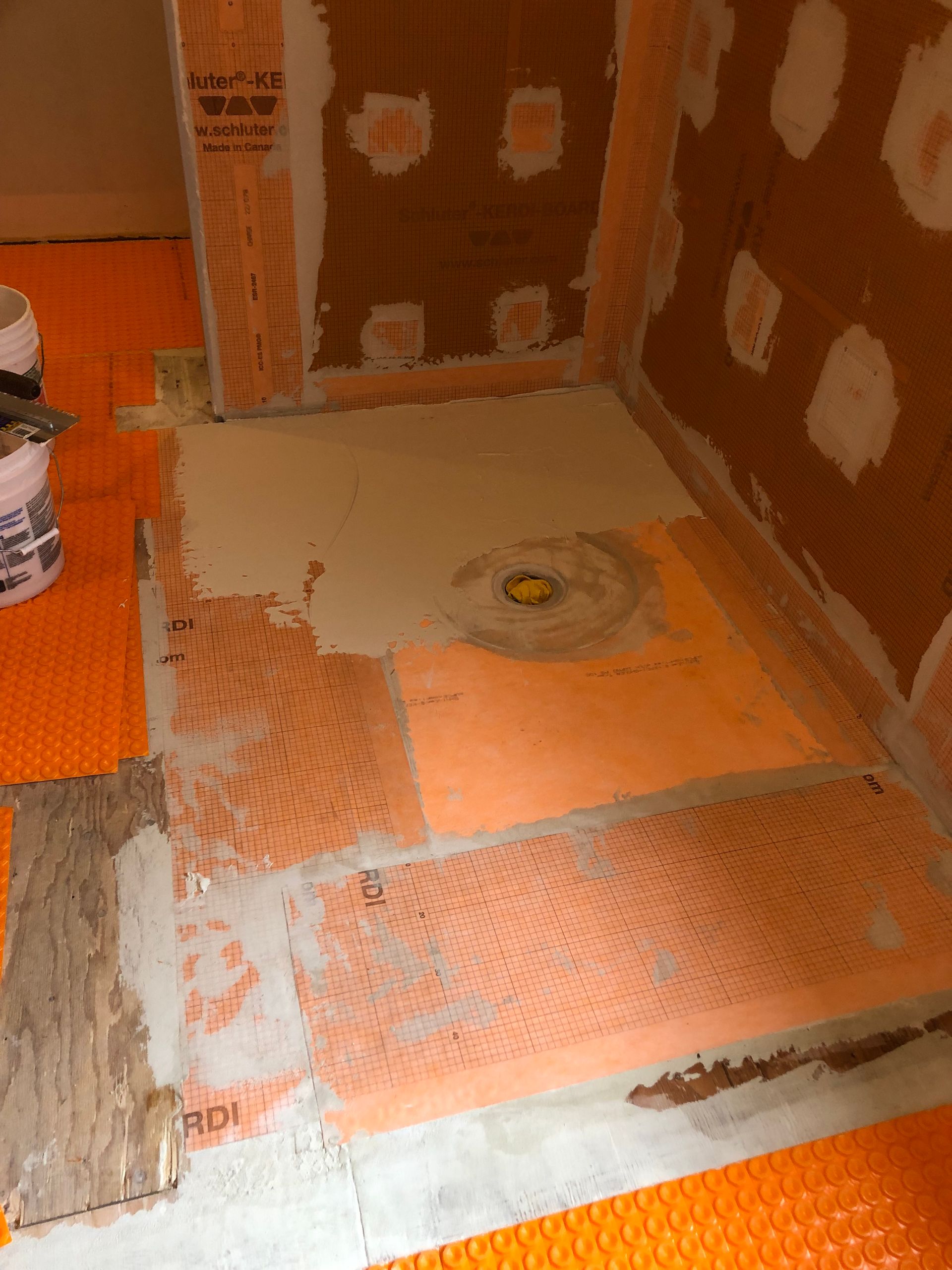 Tiled shower floor and walls mid-renovation, with orange waterproofing membrane and patchy cement board.