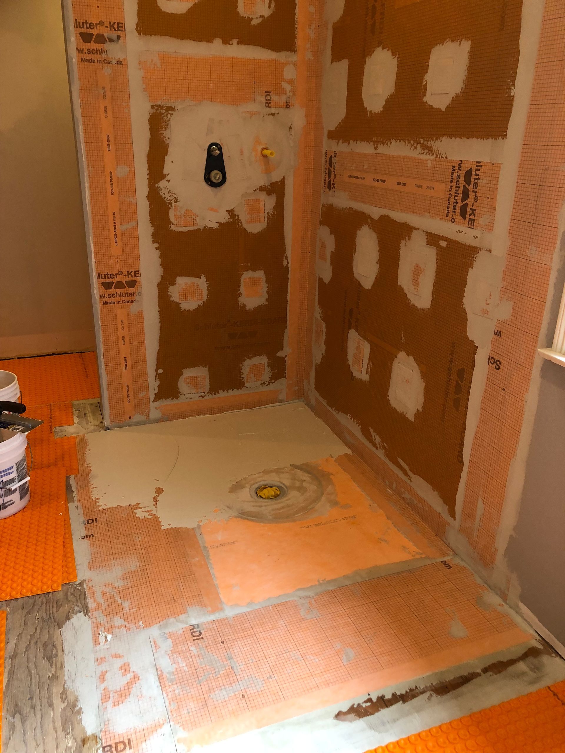 Tiled shower under construction with exposed cement board and orange waterproofing membrane.