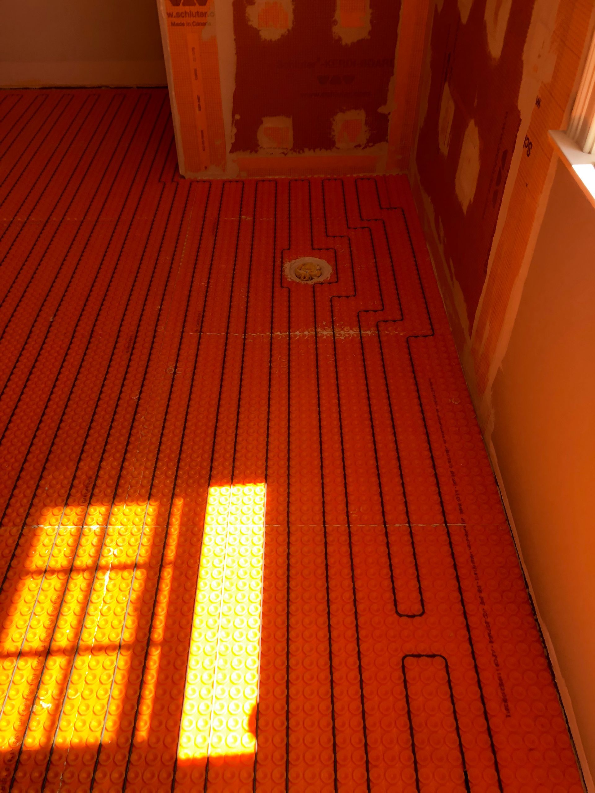 Sunlit orange floor with black striping and a small round floor fixture near the wall
