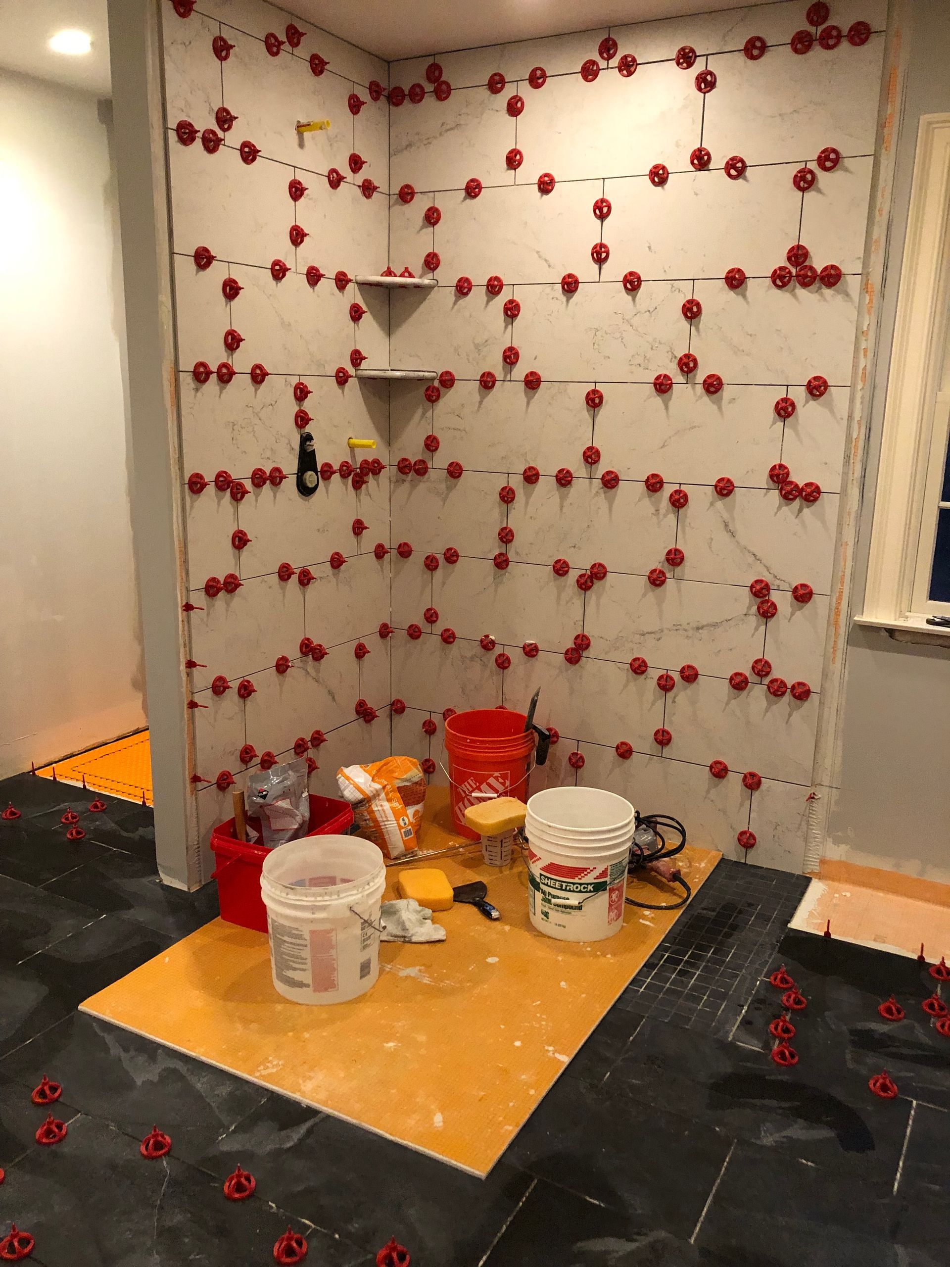 Partially renovated corner with red floral wallpaper, paint buckets, tools, and supplies on a floor tarp
