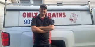 Man standing in front of a white truck with “ONLY DRAINS” and a phone number on it; arms crossed.