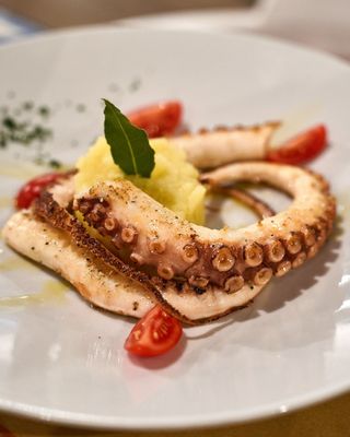 Polpo grigliato su un piatto bianco con purè di patate e pomodorini