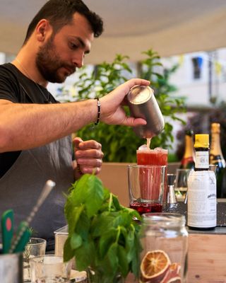 Un barista versa un cocktail in un bicchiere, con menta fresca e agrumi sul bancone.