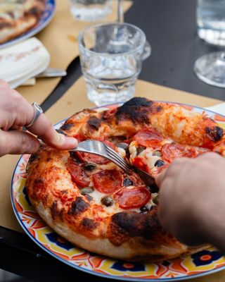 Mani che tagliano una pizza su un piatto decorato a un tavolo di ristorante.