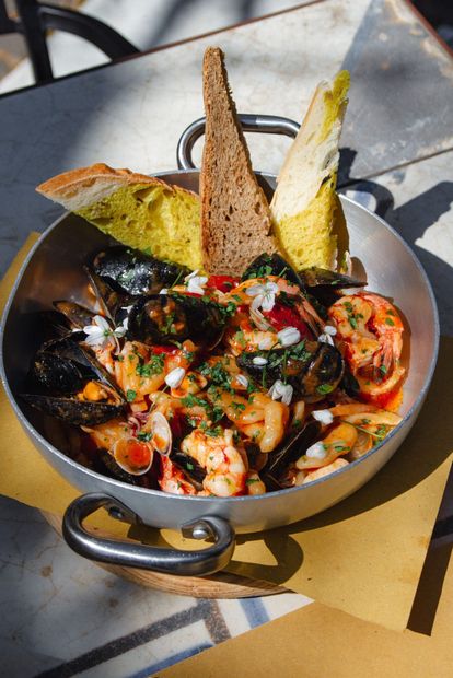 Zuppa di pesce in una ciotola di metallo con cozze, gamberi, pomodori e due fette di pane tostato.