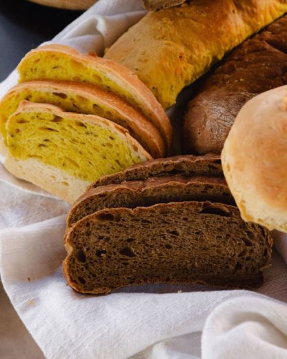 Assortimento di pagnotte di pane affettate su un panno bianco, tra cui una pagnotta di segale scura e una pagnotta di colore giallo.