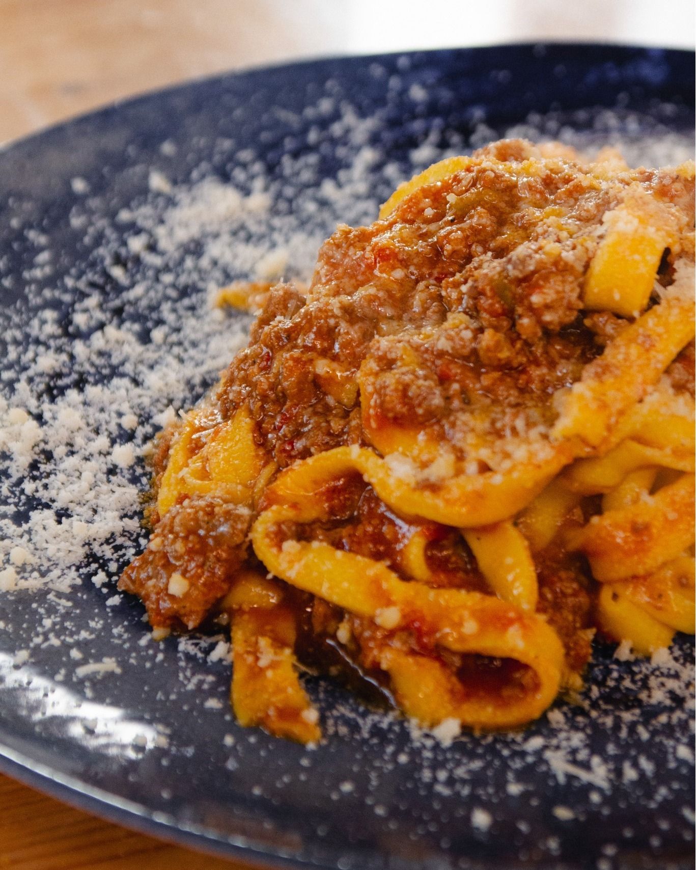 Pasta al ragù su un piatto blu scuro, cosparsa di formaggio grattugiato.