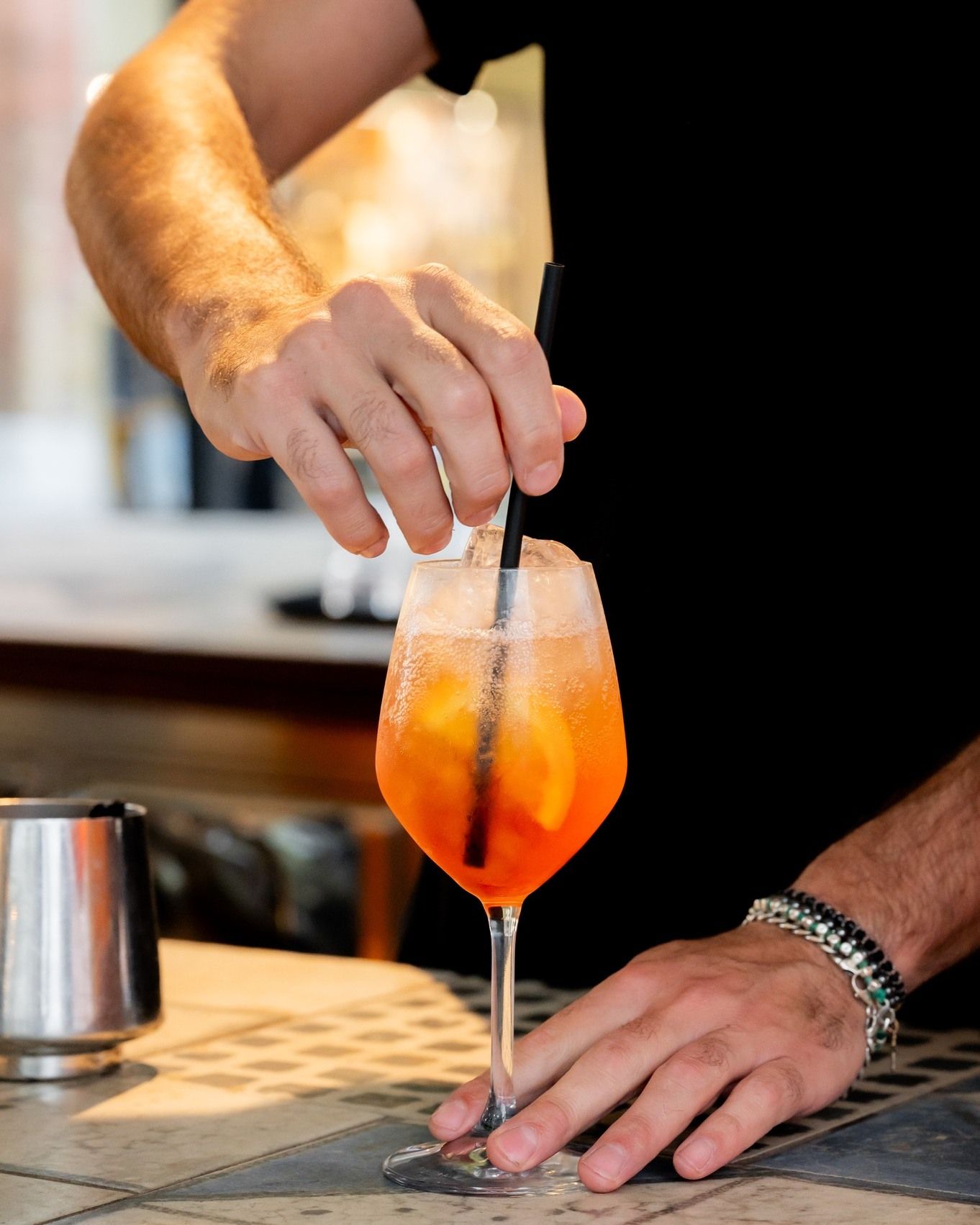 Un barista prepara un cocktail all'arancia con ghiaccio e pinze al bancone di un bar.