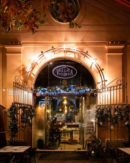 Elegante ingresso di ristorante di notte, illuminato da luci calde e con cancelli in ferro battuto, incorniciato da verde e fiori.