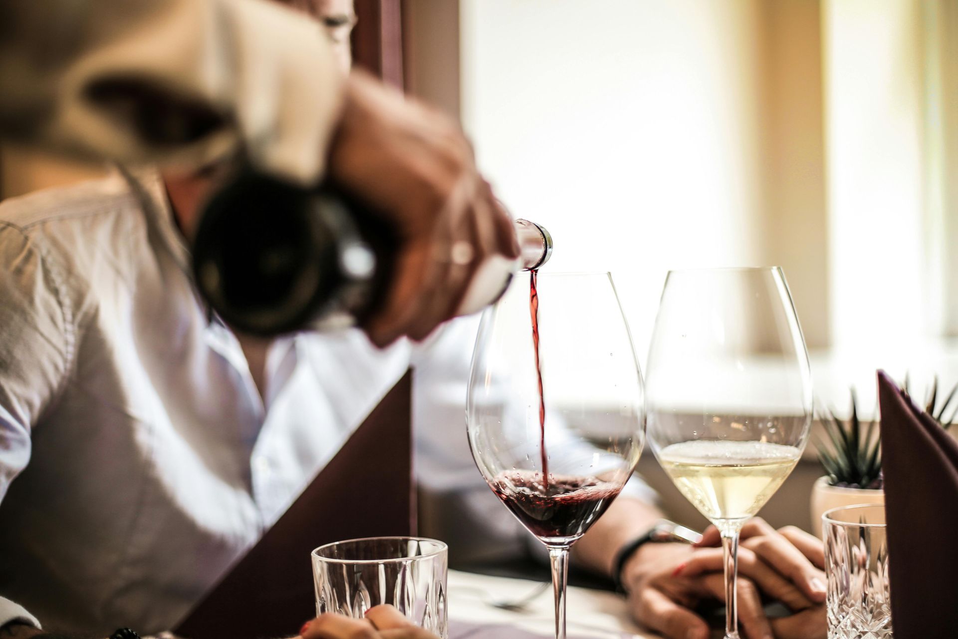 Una persona versa del vino rosso nei bicchieri a un tavolo di un ristorante.