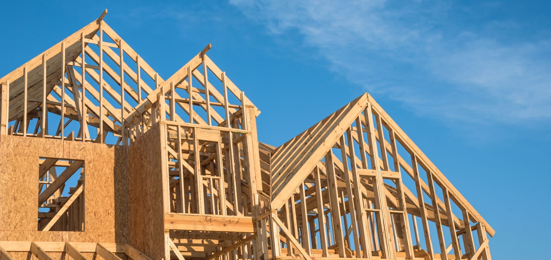 Framing of a house under construction against a bright blue sky.