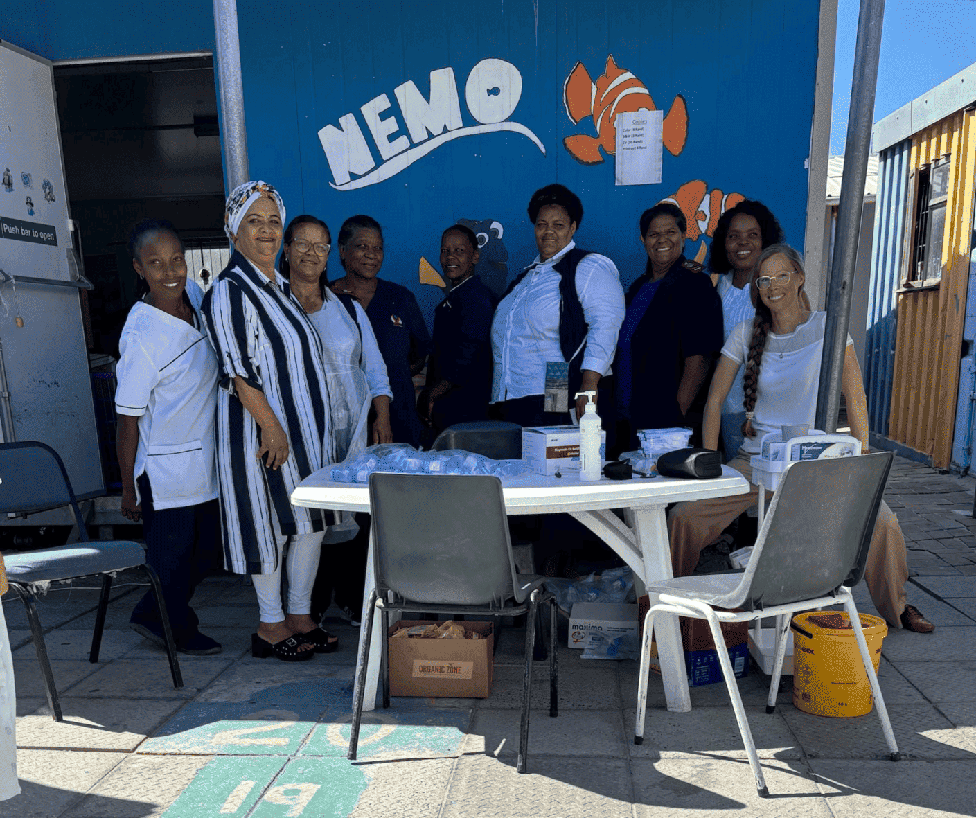 Group of people standing behind a table at an outdoor NEMO booth with a blue wall and signage.