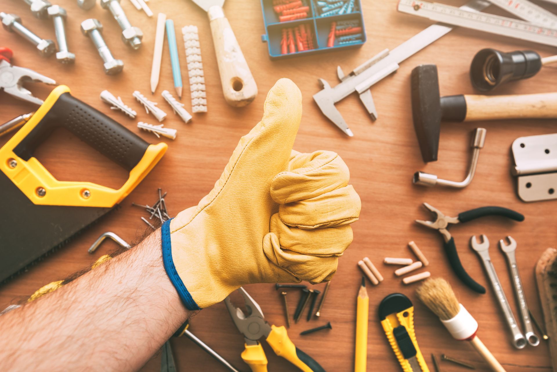 Gloved hand giving thumbs up amid assorted tools on a wooden workbench