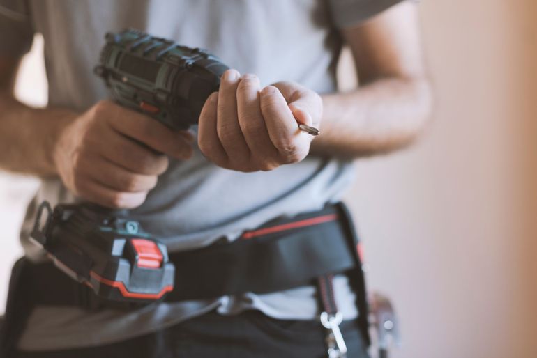 Person holding a cordless drill while fastening a black tool belt with red accents