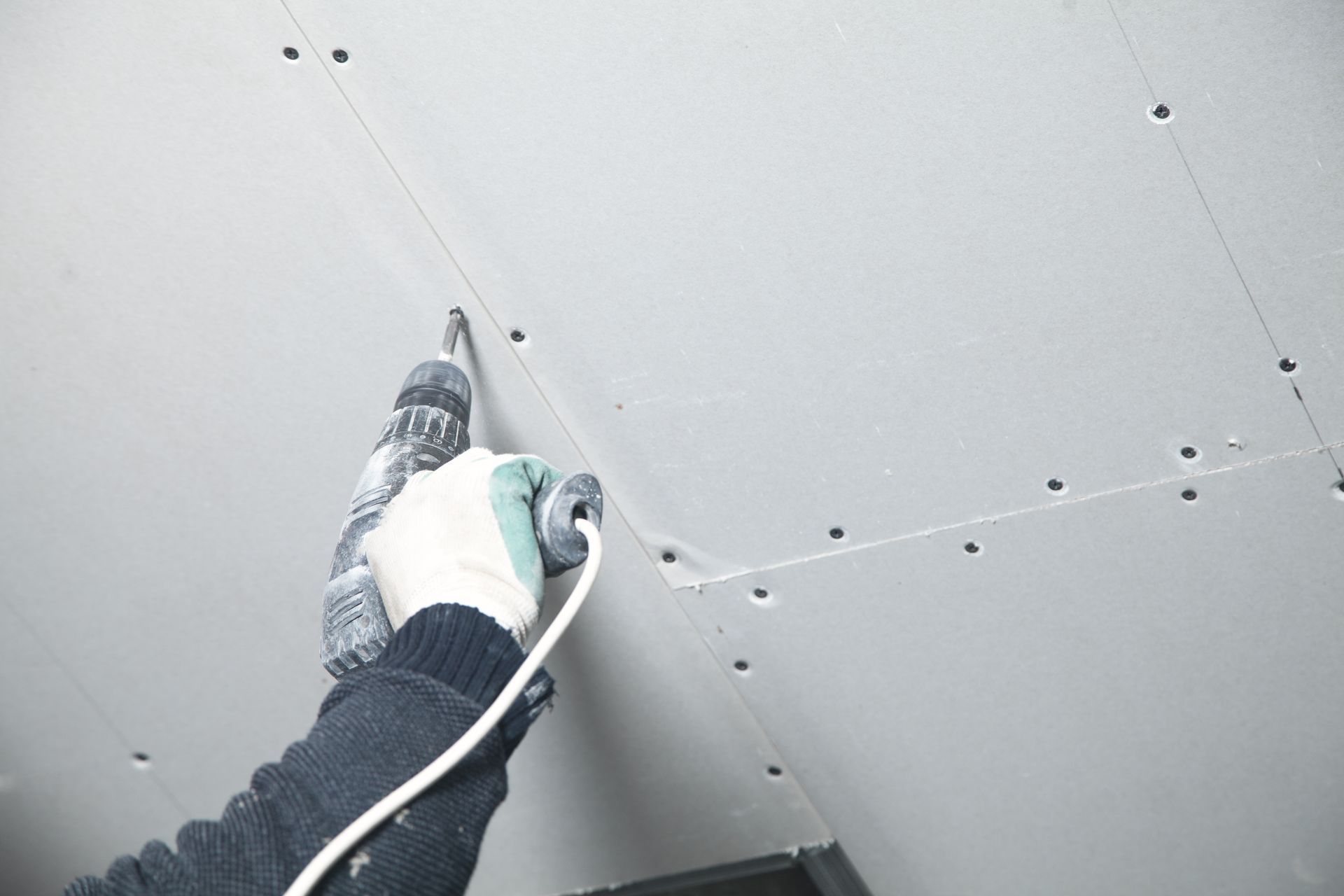 Person using a drill to install drywall screws in a ceiling panel.