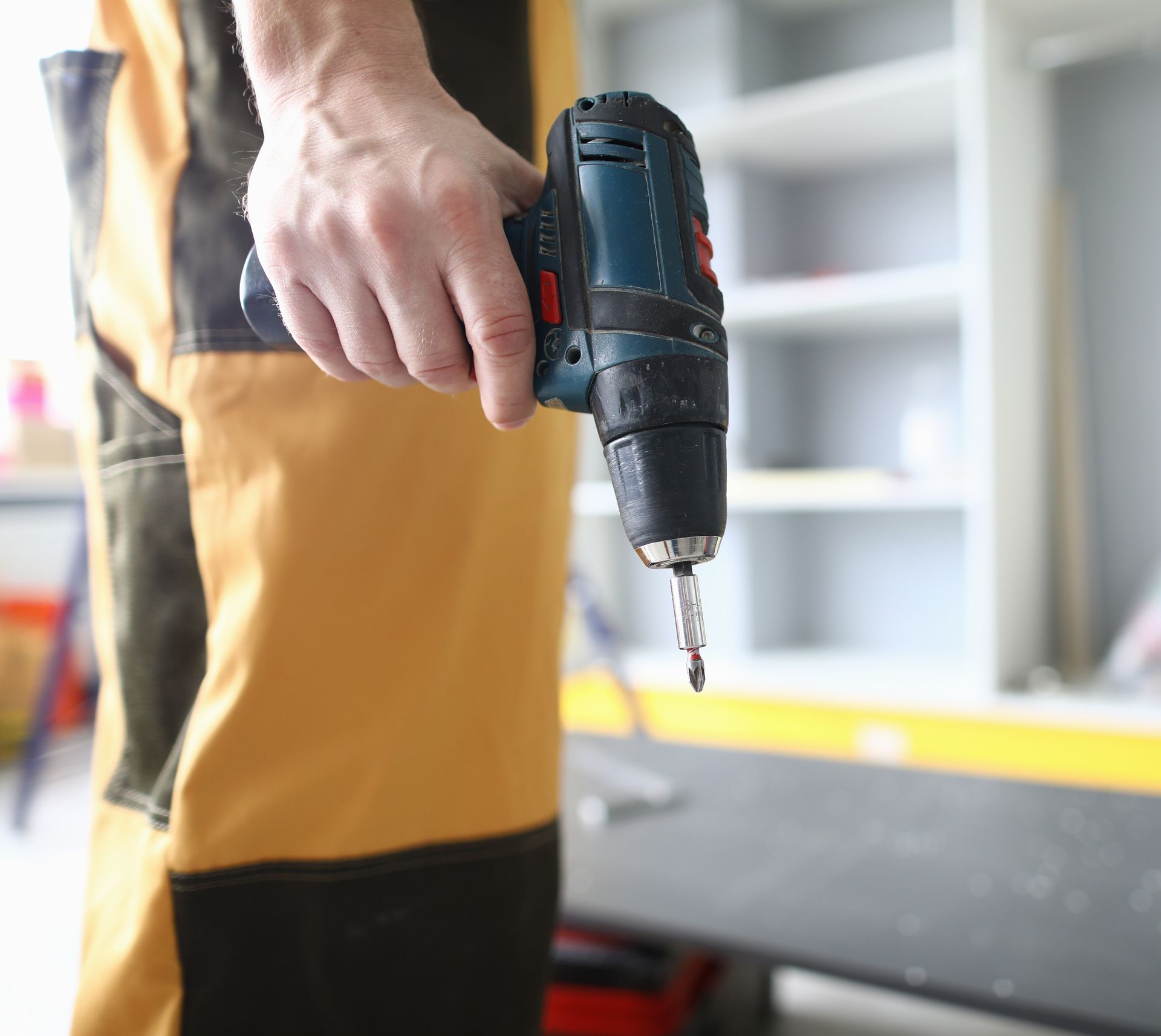 Person holding a cordless drill in a workshop, ready to drill into a workbench.