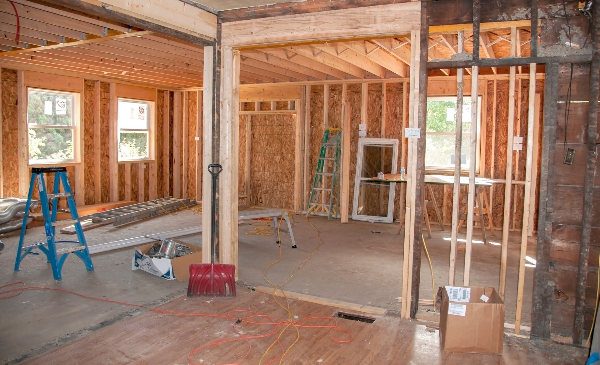 Interior of a house under renovation with exposed framing, ladders, tools, and unfinished drywall
