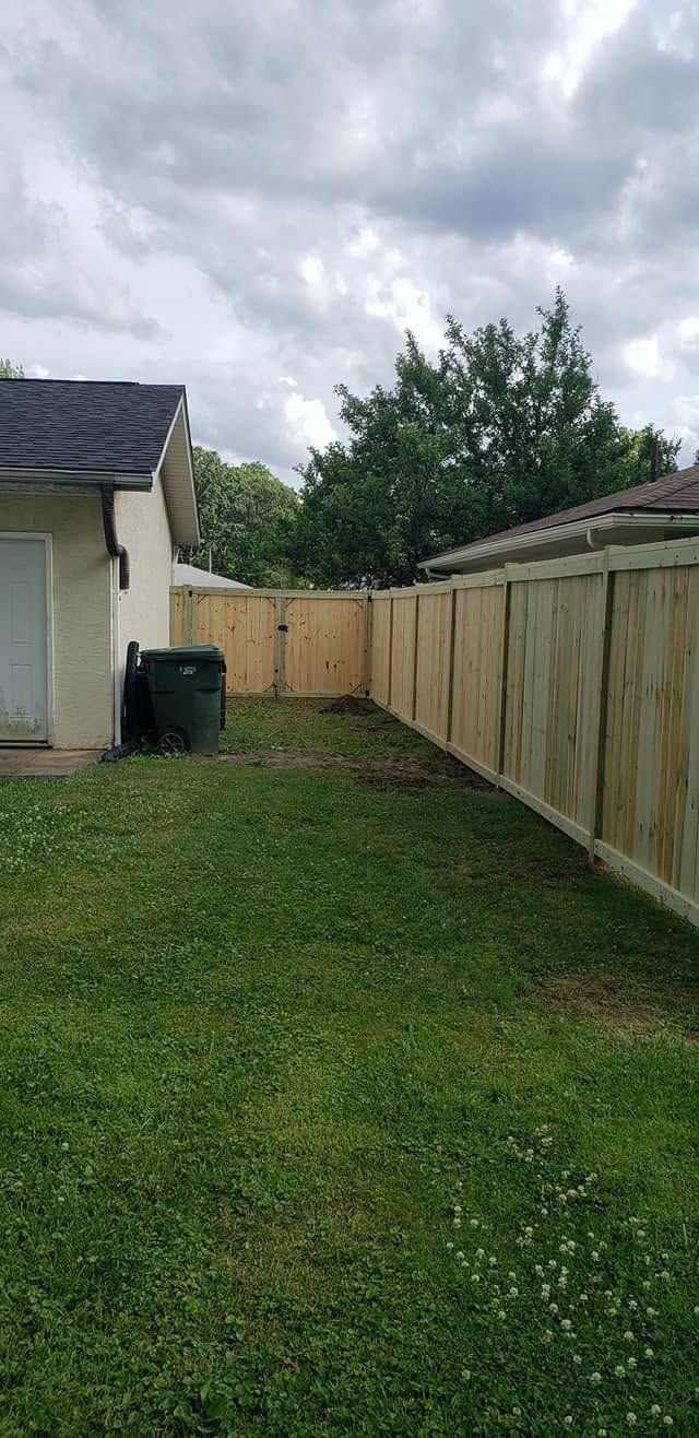 Narrow backyard with grass, tall wooden fence, and cloudy sky beside a house and shed.