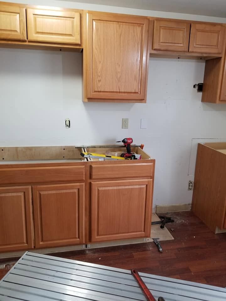 Partially renovated kitchen with wooden cabinets, white walls, and exposed appliances on the floor