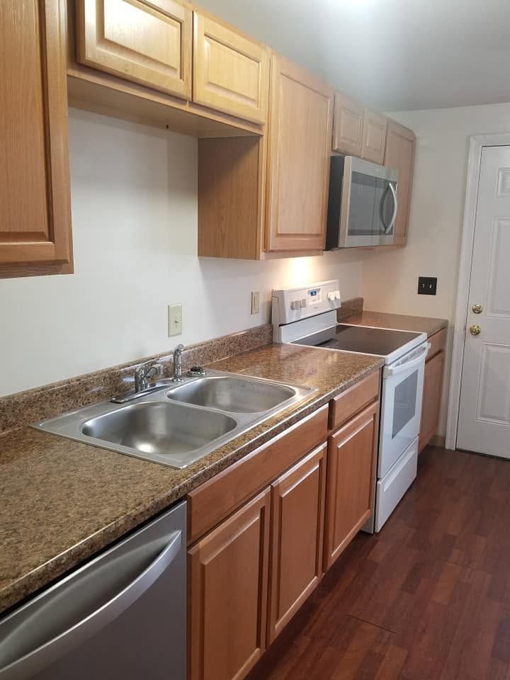 Modern kitchen with wooden cabinets, granite countertops, stainless sink, dishwasher, stove, microwave, and wood floor