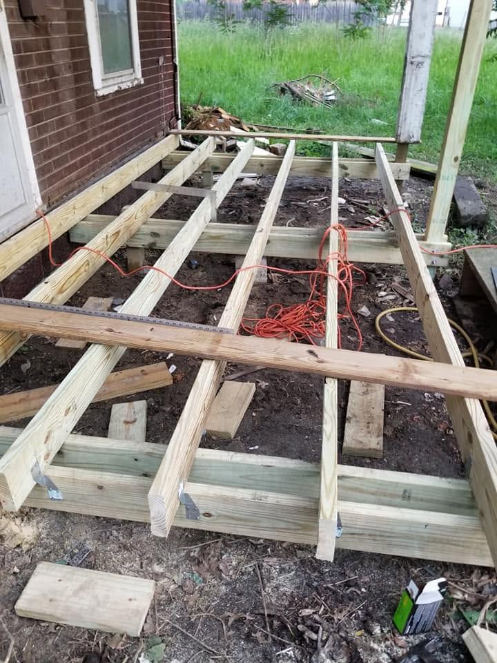 Partially built wooden deck frame beside a brick house, with exposed joists and support posts