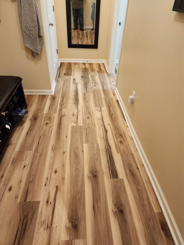 Narrow hallway with light wood flooring, beige walls, and a framed picture at the far end.