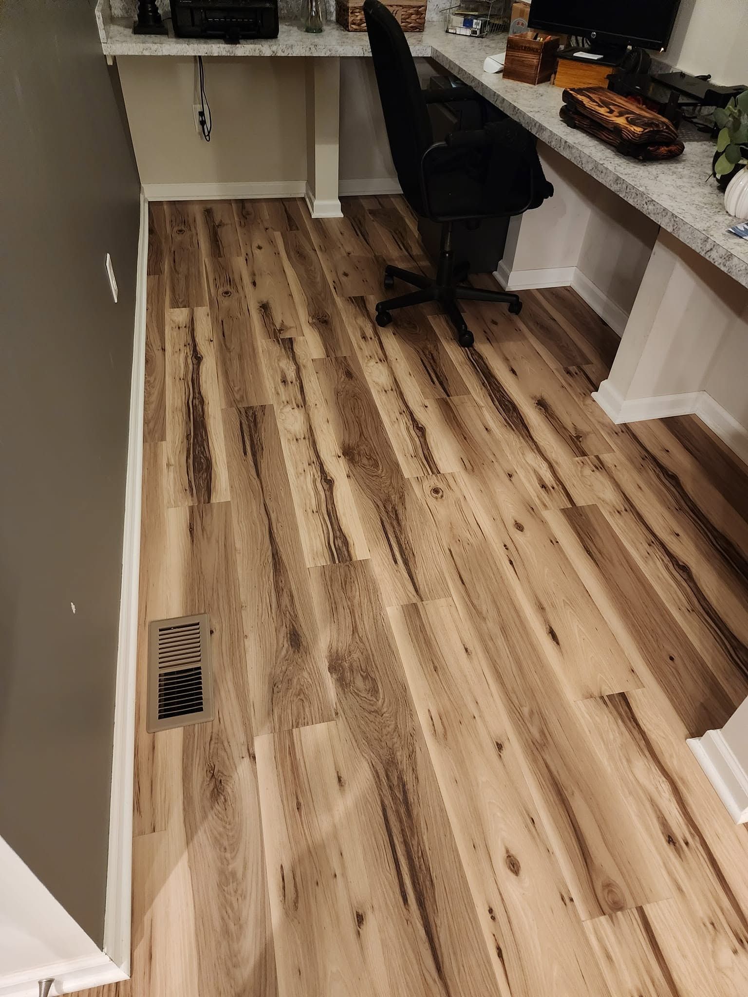 Empty room with light wood flooring, white desk, and black office chair near a countertop.
