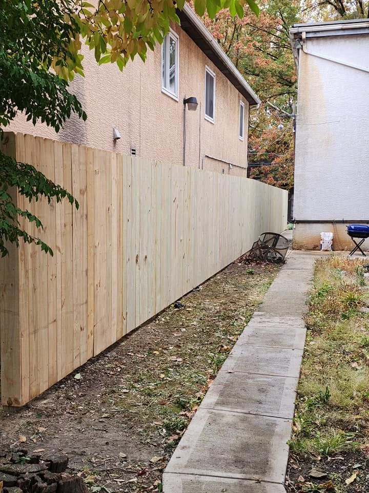 Narrow side yard with a newly installed wooden privacy fence beside a house and concrete walkway