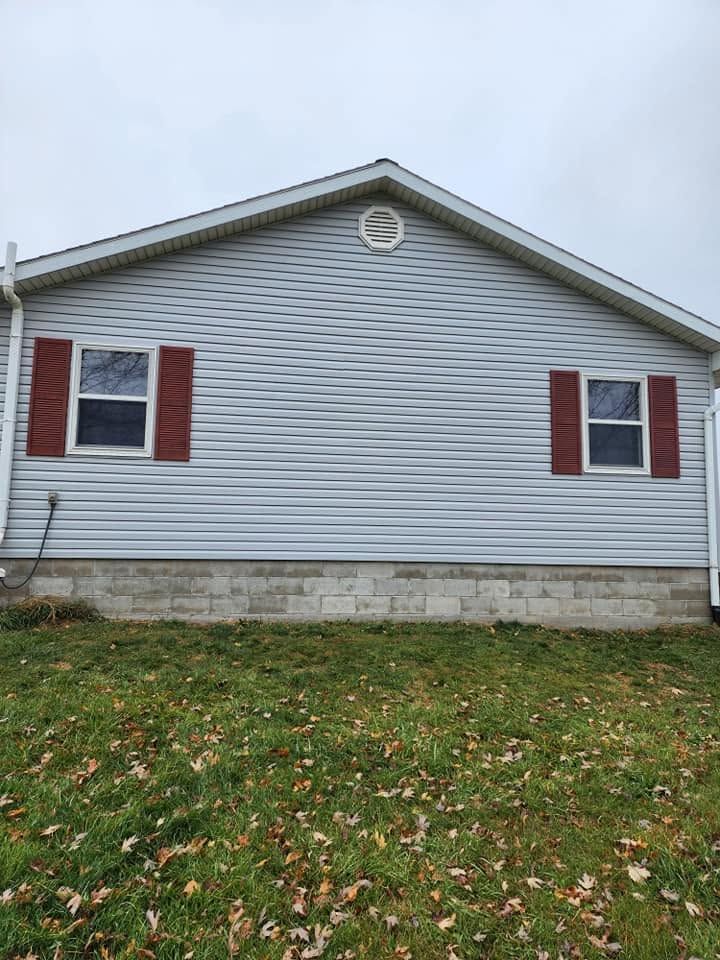 Gray house exterior with red shutters and a small circular attic vent above a stone foundation
