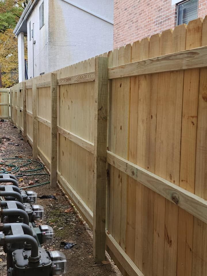 Wooden privacy fence along a house beside a narrow dirt path and outdoor equipment run