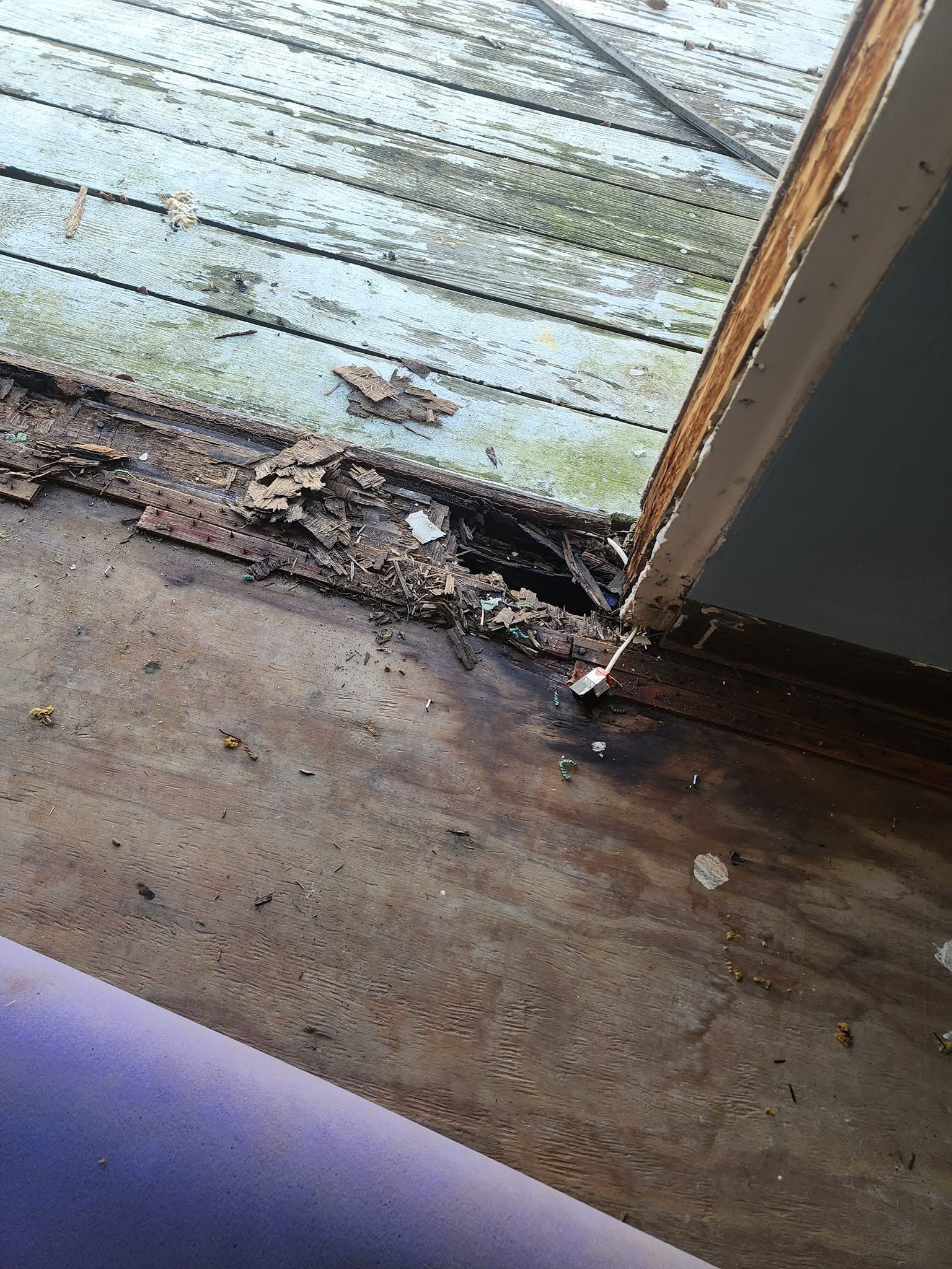 Damaged wooden floorboards at a doorway with rotting, broken wood and peeling paint