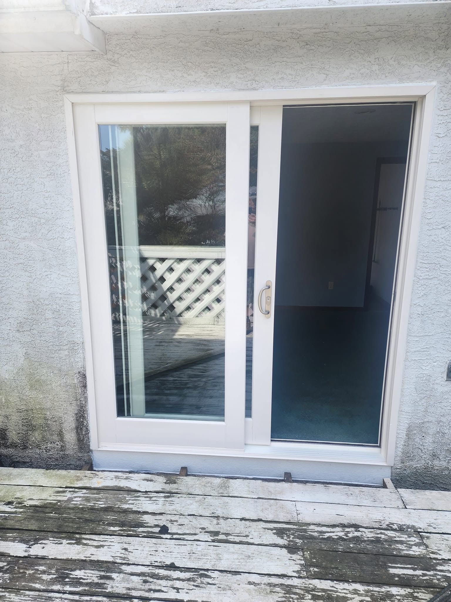 White sliding glass patio door with one panel open to a dark interior, on a weathered deck.